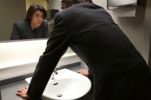 A person wearing a business suit and leaning forward, looking a bathroom mirror. Source: Getty Images
