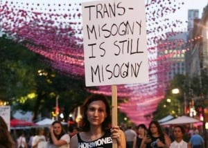 A person in a crowd holds a sign reading "transmisogyny is still misogyny."