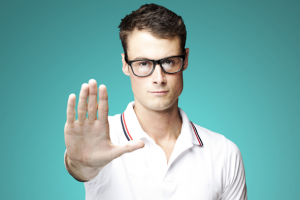 A person with glasses and a polo shirt holds their palm up toward the camera. Source: 1213 Online