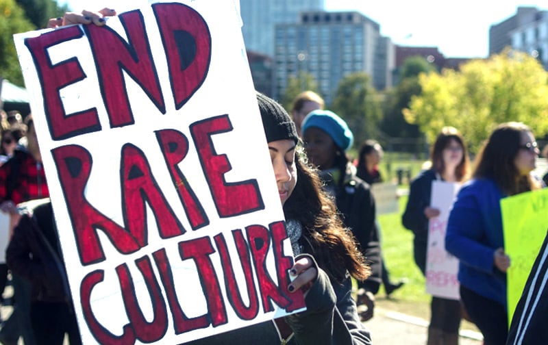 A person at a demonstration holds a sign reading "End rape culture."