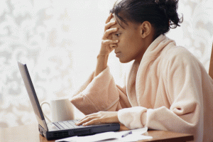 A tired person in a robe looking at a computer screen with their hand over their face. Source: Young Mommy Life