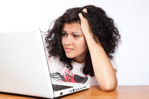 A person with their hand in their hair frowns at a laptop computer in frustration.