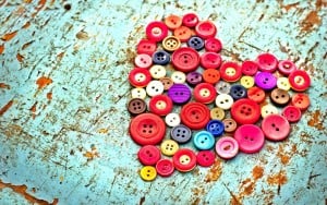 A collection of colorful buttons make a heart shape over a distressed teal table top