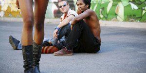 Two people sitting on the ground, catcalling someone walking by