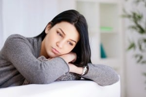 Person sitting on a couch, leaning against their own arms, looking worried or contemplative
