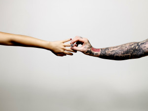 One tattooed arm outstretched to place an engagement ring on the finger attached to another outstretched arm