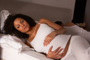 Pregnant person lying on a bed, looking concerned