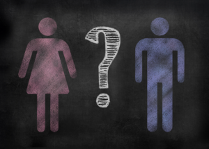 Pink "woman" symbol and blue "man" symbol drawn on a chalkboard with a question mark in the middle