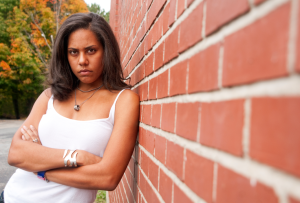 Young person leaning against a wall with their arms crossed, angry