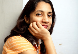 A person gazes at the camera with their hand on their chin and a small smile
