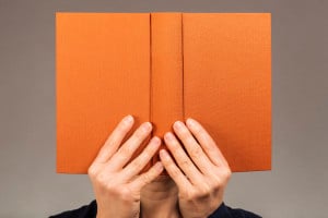 Person holding up an orange book, hiding behind it, deep in reading