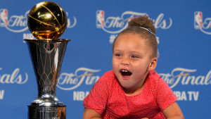 Riley Curry smiling beside the NBA championship trophy