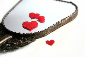 A handheld mirror lays against a table with cut-out red paper hearts strewn about