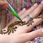 A hand is set against a table, being adorned with henna