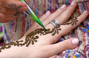 A hand is set against a table, being adorned with henna