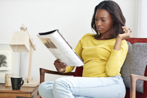 A person in a yellow shirt and light jeans reading a magazine