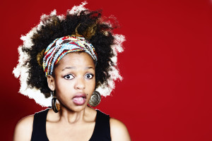 A person with an afro and headscarf with a surprised facial expression