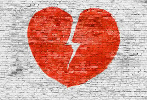 A red broken heart is painted on a white brick wall