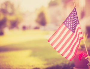 An American flag is pictured, sitting in a flower pot outside of a suburban home