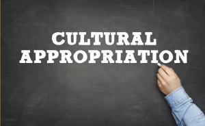 A chalkboard reads "Cultural Appropriation," as if it's the lesson of the day