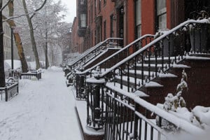 Snow covered Brooklyn brownstone townhouse stoops and sidewalk in winter. Snow is falling during a late winter storm in the Brooklyn Heights Historic District. Gardens, stoops, and sidewalks are covered in deep snow. Selective focus on the stoop steps.