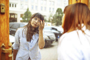 A person looking in a mirror on the street, fixing something on their face
