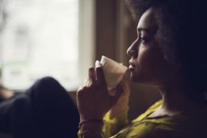 Pensive person, looking out a window, holding a warm drink