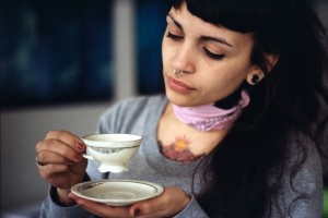 A person with tattoos, drinking from a small, porcelain tea cup