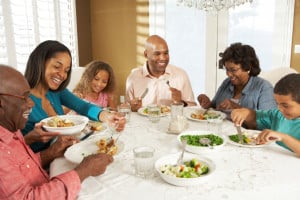 A family passes food dishes around the table, enjoying their meals and smiling.