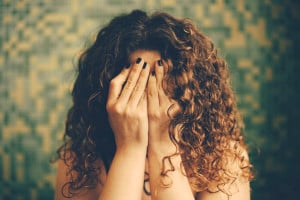 A person with curly hair covering their face with their hands.