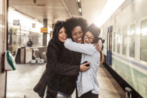 Three friends are hugging at a train station.