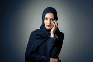 A person wearing hijab looks straight on into the camera, appearing pensive, their hand touching their face.
