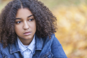 A young person stares off into the distance on a fall day, looking worried or thoughtful.