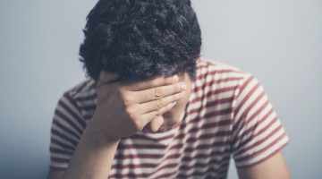 A sad young man is resting his head in his hand