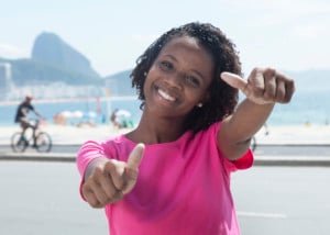 African american woman at Rio de Janeiro showing thumb with Sugarloaf mountain and Copacabana beach in the background