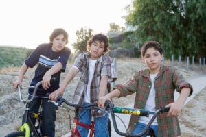 Three young people sit on their bikes, hands resting on the handle bars, staring at the camera with a dissatisfied expression.