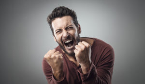 A person holds up clenched fists while they yell with a strained expression.