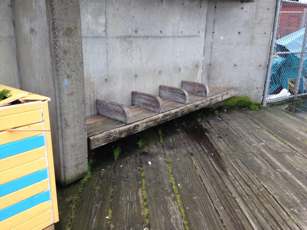 A wood bench with dividers tucked away against a concrete wall.