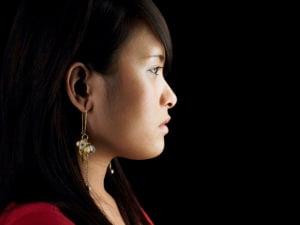 Profile of someone on a black background. They have long black hair, dangling gold earrings, and a serious expression.