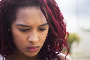 Closeup on a person with red hair and a nose piercing looking down with a sad expression.