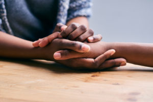 Closeup of two sets of hands holding each other from across a table.