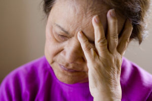 An elderly person covers half their face, appearing upset and defeated.
