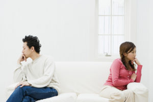 Two people sitting on a couch, looking in opposite directions, seeming to ignore one another.