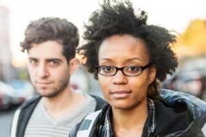Closeup on two people standing on a street, staring into the camera.