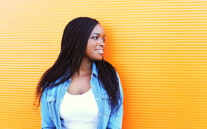 A young person turns their head to smile and look at something next to them. They stand against a bright orange background.