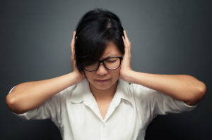 A person with a stressed expression covers their ears with their hands.