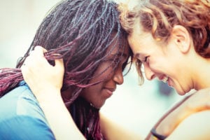 Two people press their foreheads together, smiling and holding one another.