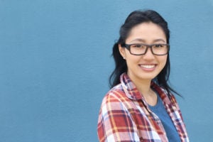 A person in a plaid shirt and glasses smiles into the camera.