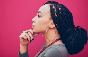 Profile shot of a person posing with their hand touching their chin against a pink background.