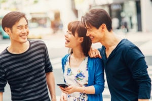 Three people smiling at one another as they walk down a street together.